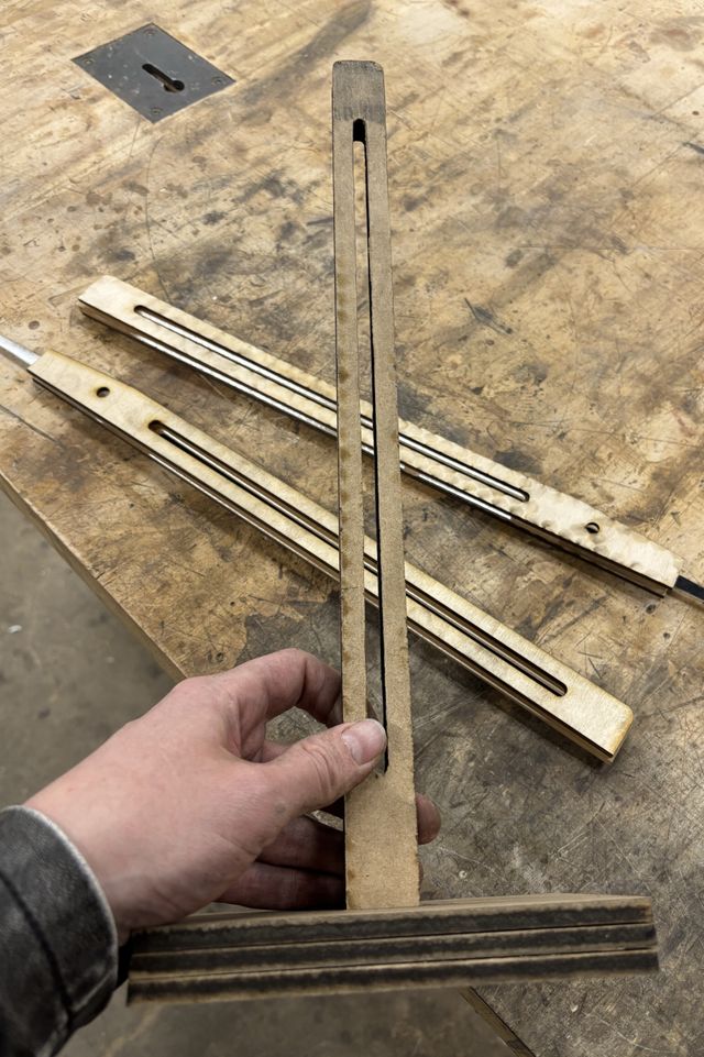 Holding up the assembled frame, 2 identical uprights slotted through a three-layer base. The uprights also have a vertical slot for adjusting the arms up and down. The assembled arms with pointer ends are on the table behind the frame.