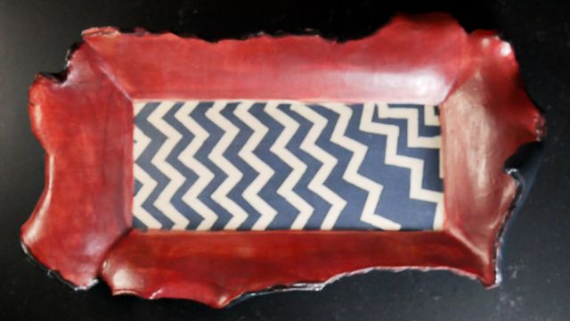 Rectangular tray with a black and white zig-zag pattern that starts tidy on the left then skews wildly on the right - the lip of the tray is red and folds over itself ending in torn edges
