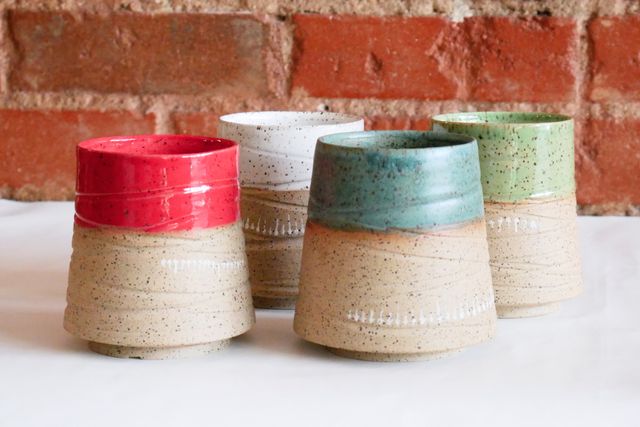 Four 12oz tumblers with a deep inset foot ring, wide base, and grooved speckled walls sloping in to a narrower brightly glazed lip - one red, one green, one blue, and one white
