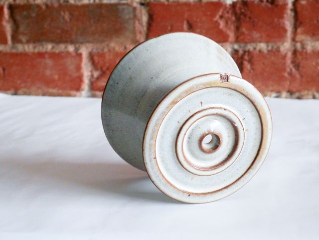The pour-over from underneath, showing a glazed base with concentric outer and inner rings around the funnel to keep the mug in position and the coffee flowing into the mug. My 'm' stamp stands out on the rim, dark clay unglazed

