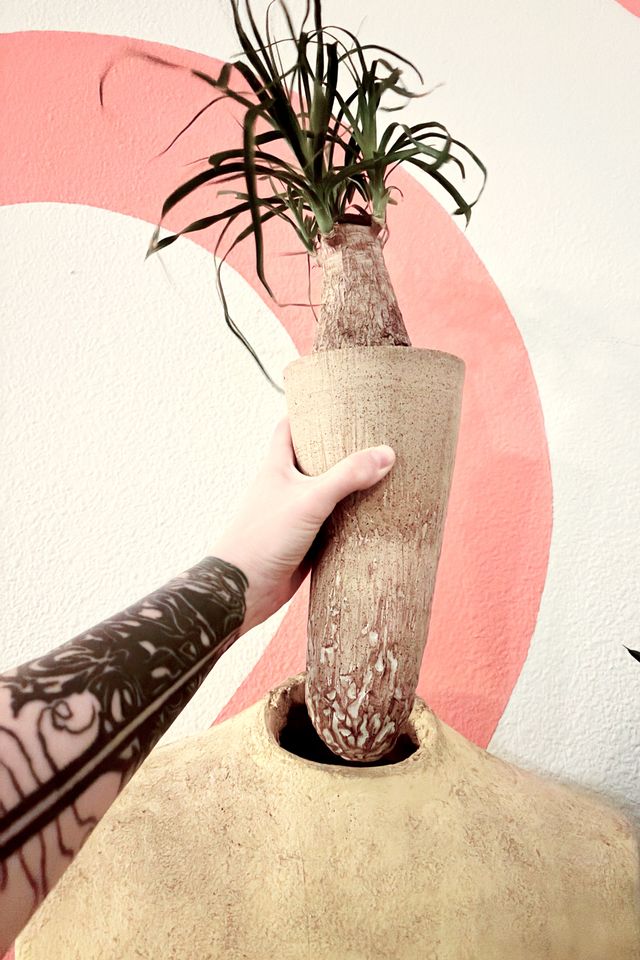 My arm reaches in to hold the coroner head out of the dress form, revealing a long bent cone with deep texture and pooled white glaze at the rounded-off base which would not be able to sit in any other location
