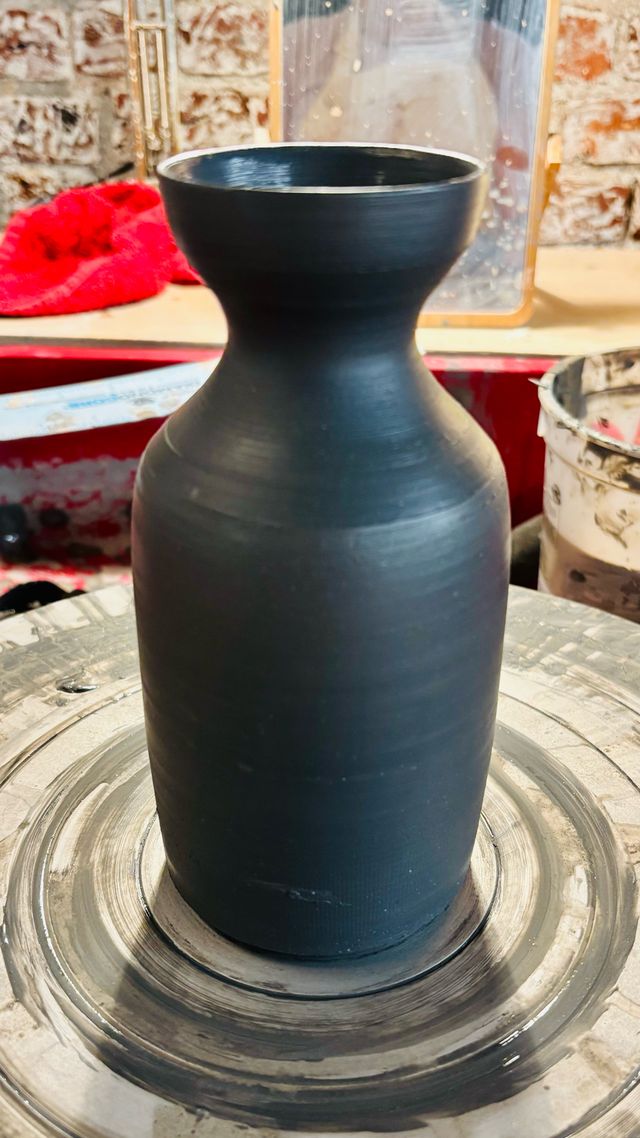 A medium-size sake bottle in coal black clay, still wet on the wheel, with a barely rounded belly, narrow neck, and cup-like rim
