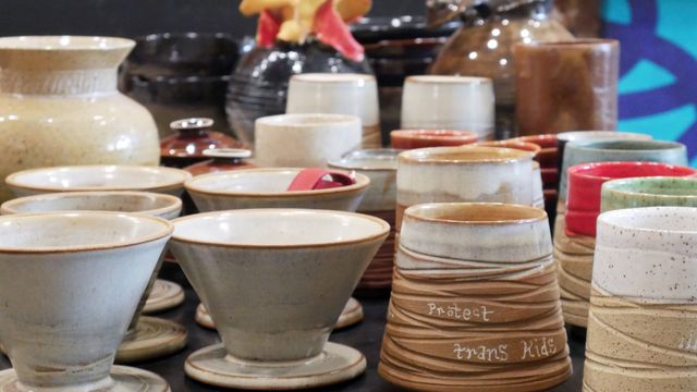 A whole set of mugs and pour-overs, gaiwan, vases, and other assorted pieces laid out on the counter. Towards the back are taller vases out of focus.
