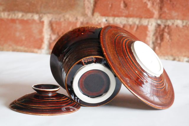 Overturned parts of the gaiwan, a lid on the table, the bottom of the bowl shows a bare white clay foot ring and my 'm' stamp, and the saucer now leaning against it has a matching grooved pattern on the underside and matching white foot-ring
