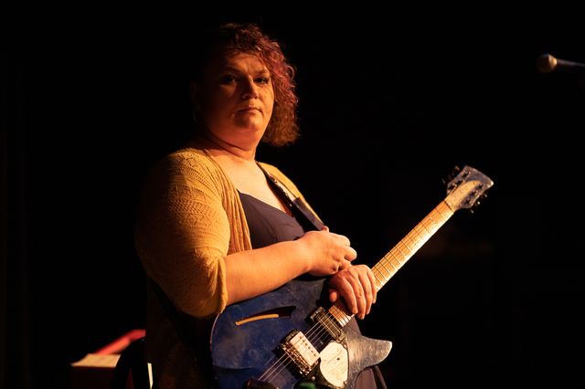 Josie sitting with a guitar,
looking at the camera
